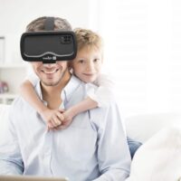 Ein sehbeeinträchtigter Mann trägt die elektronische Lupenbrille Acesight VR um in die Ferne zu sehen. Hinter ihm ist sein Kind zu sehen.